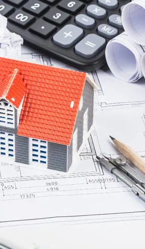 A model house beside a calculator and blueprints